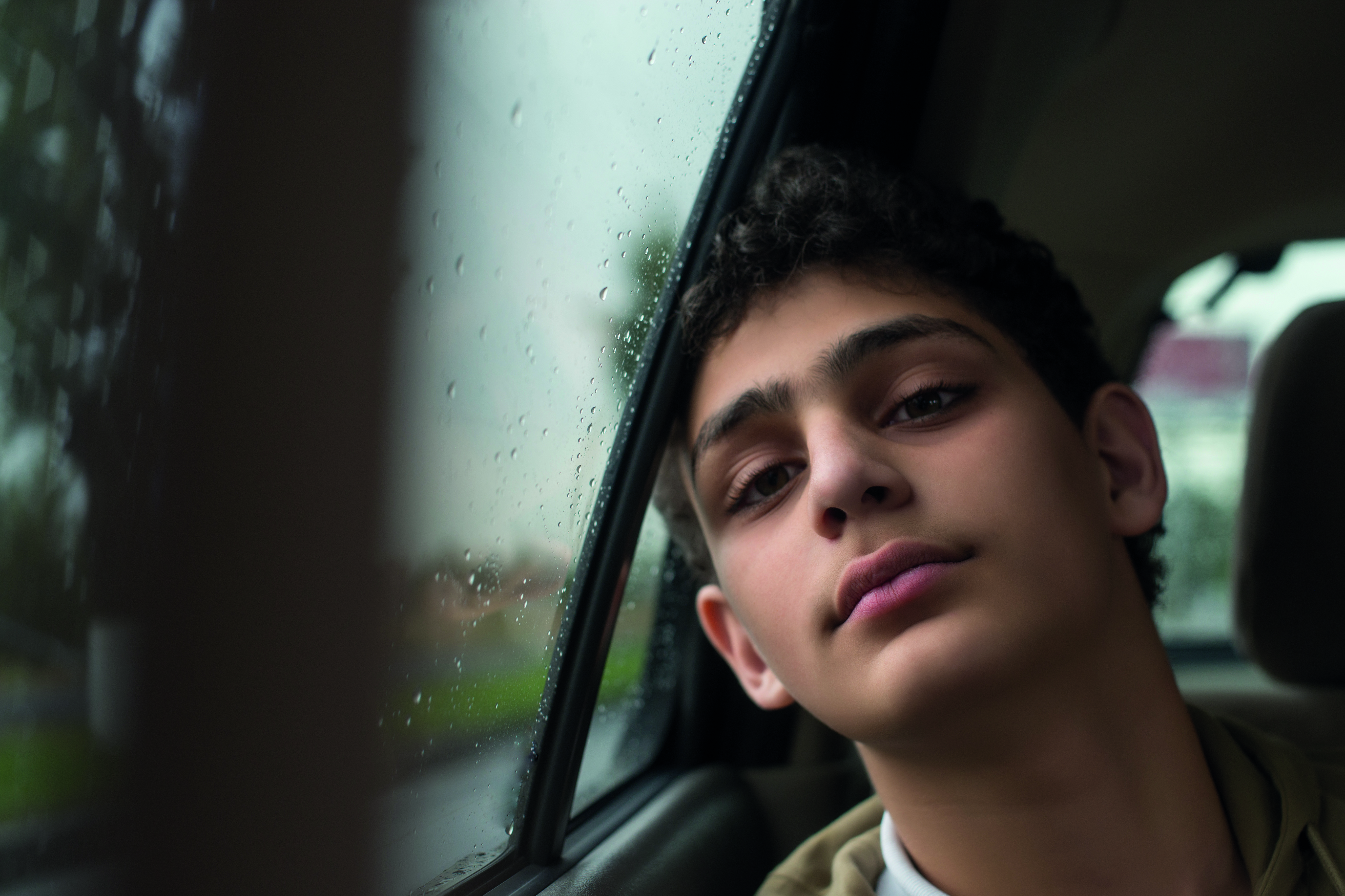Teenage boy sitting in a car leaning his head on the window