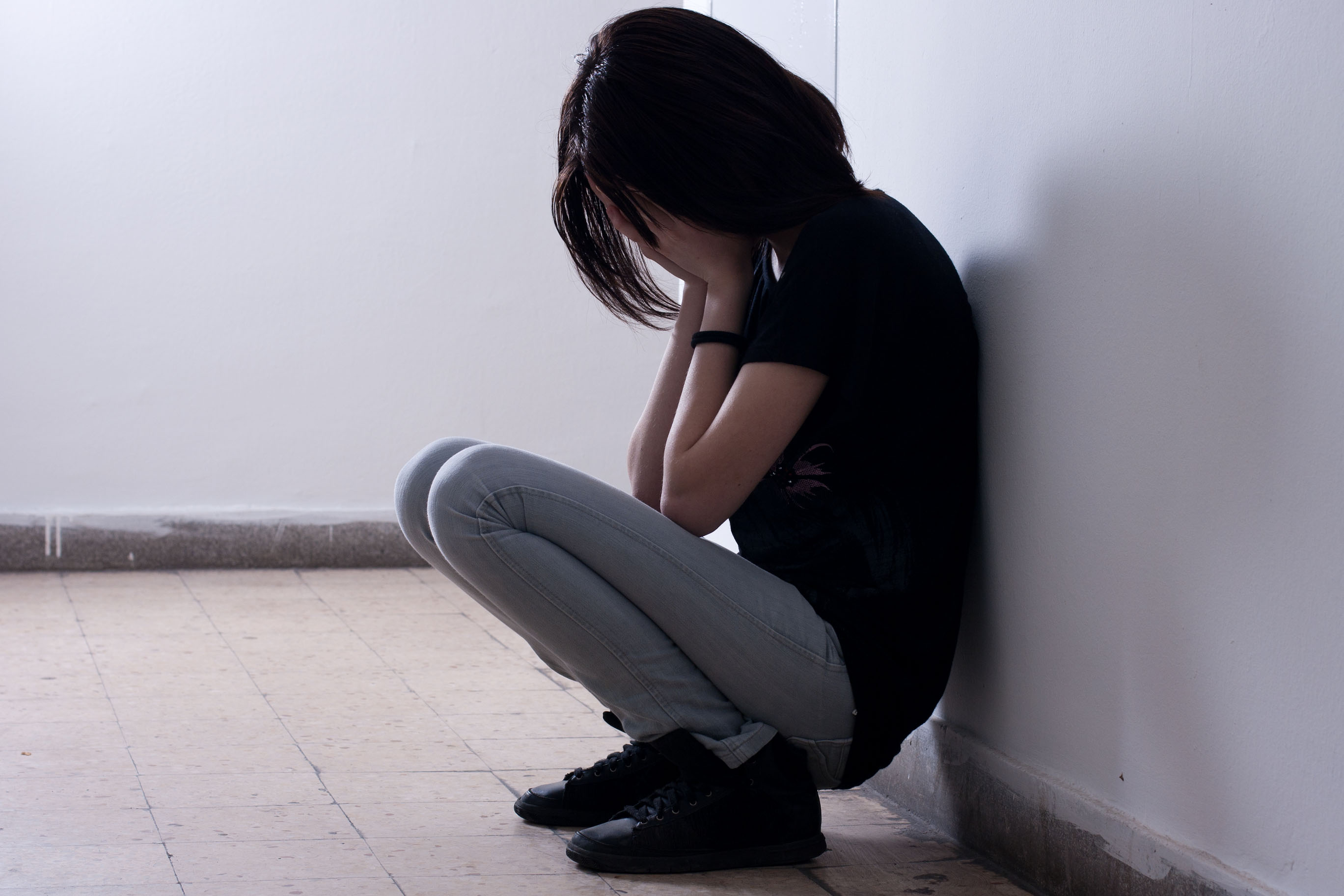 Girl crouching against a wall with her head in her hands